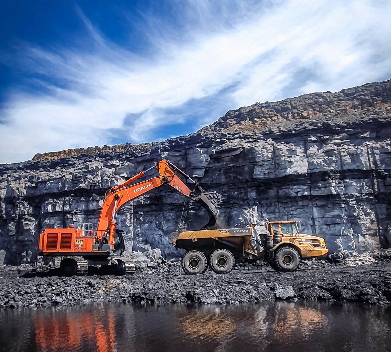 An orange excavator loading a yellow dump truck at a quarry in Mpumalanga, South Africa.
